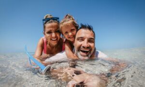 mother, father and daughter take a selfie while soaking in beach water