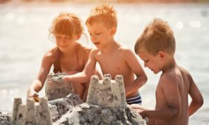 three kids build a sand castle on a beach