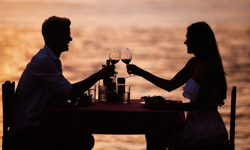 couple putting wine glasses together at a beach dinner table